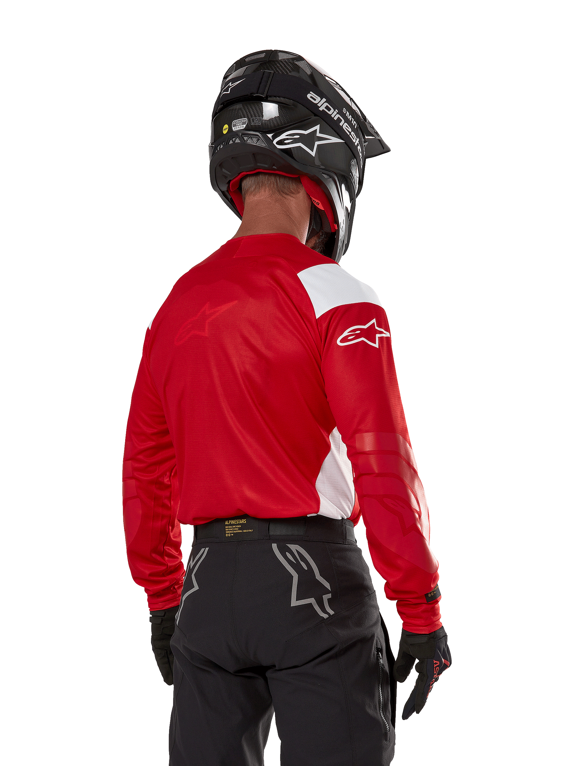 Motocross rider seen from the back wearing the Alpinestars Techdura Jersey in Bright Red with white panels, paired with black off-road pants, a black helmet, and black gloves, coordinated gear for enduro and motocross riding.