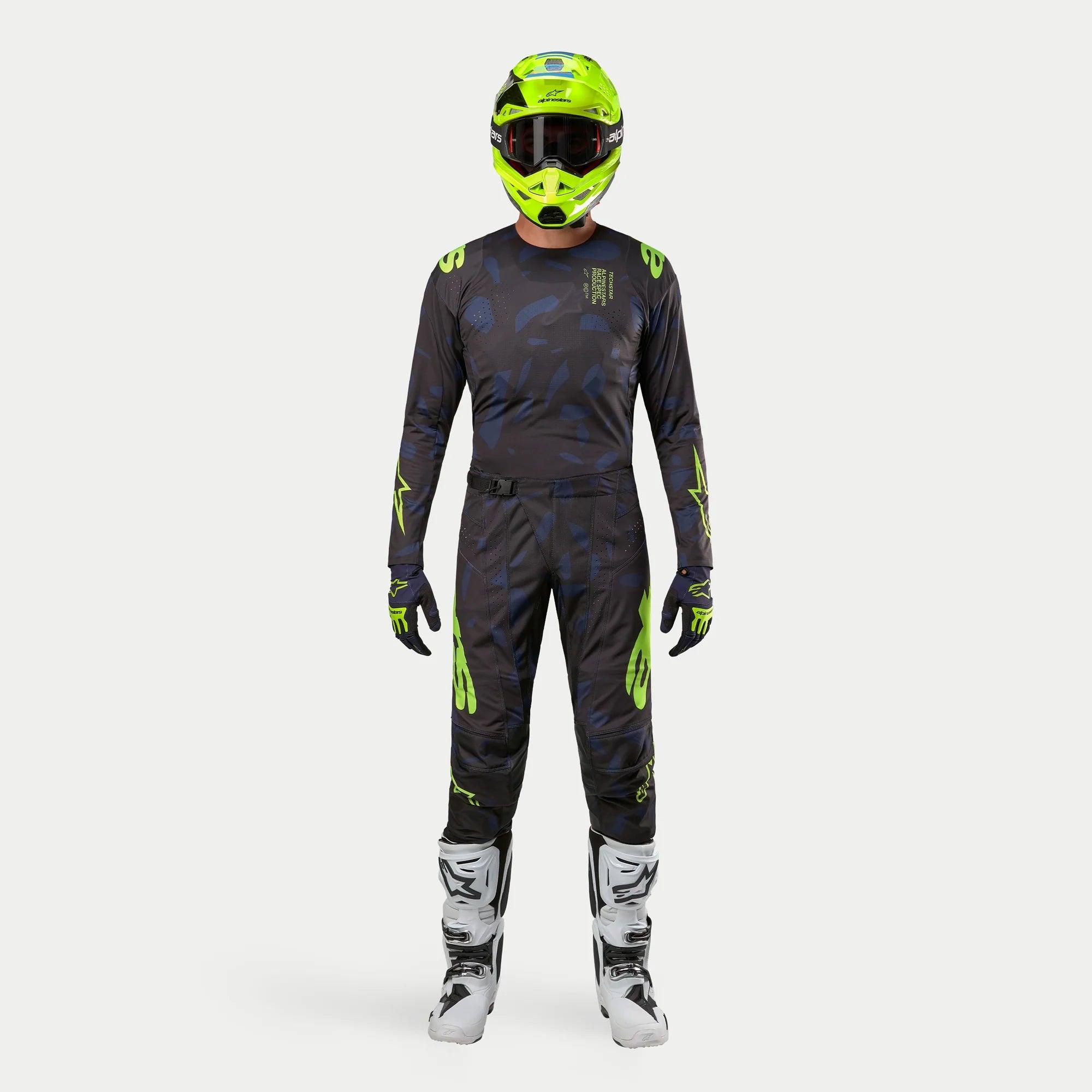 Motocross rider wearing complete racing gear, 2024 Techstar Rantera Jersey in Black Navy and Yellow Fluo, matching abstract print pants, bright fluo yellow helmet, white and black boots, coordinated outfit for off-road racing