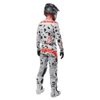 Piloto de motocross visto desde atrás con el jersey Alpinestars Techstar Rantera 2024 y pantalones a juego, patrón de camuflaje Haze Gray con logotipos rojos llamativos de Alpinestars, casco negro, botas blancas y negras, guantes negros, conjunto coordinado de equipamiento de motocross