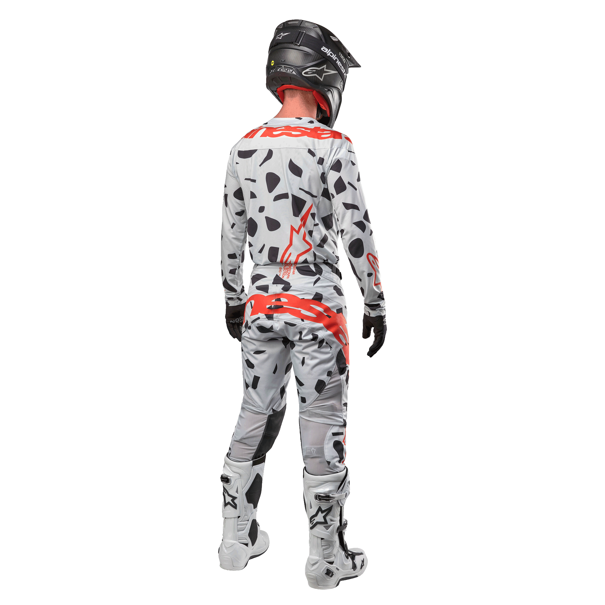 Piloto de motocross visto desde atrás con el jersey Alpinestars Techstar Rantera 2024 y pantalones a juego, patrón de camuflaje Haze Gray con logotipos rojos llamativos de Alpinestars, casco negro, botas blancas y negras, guantes negros, conjunto coordinado de equipamiento de motocross