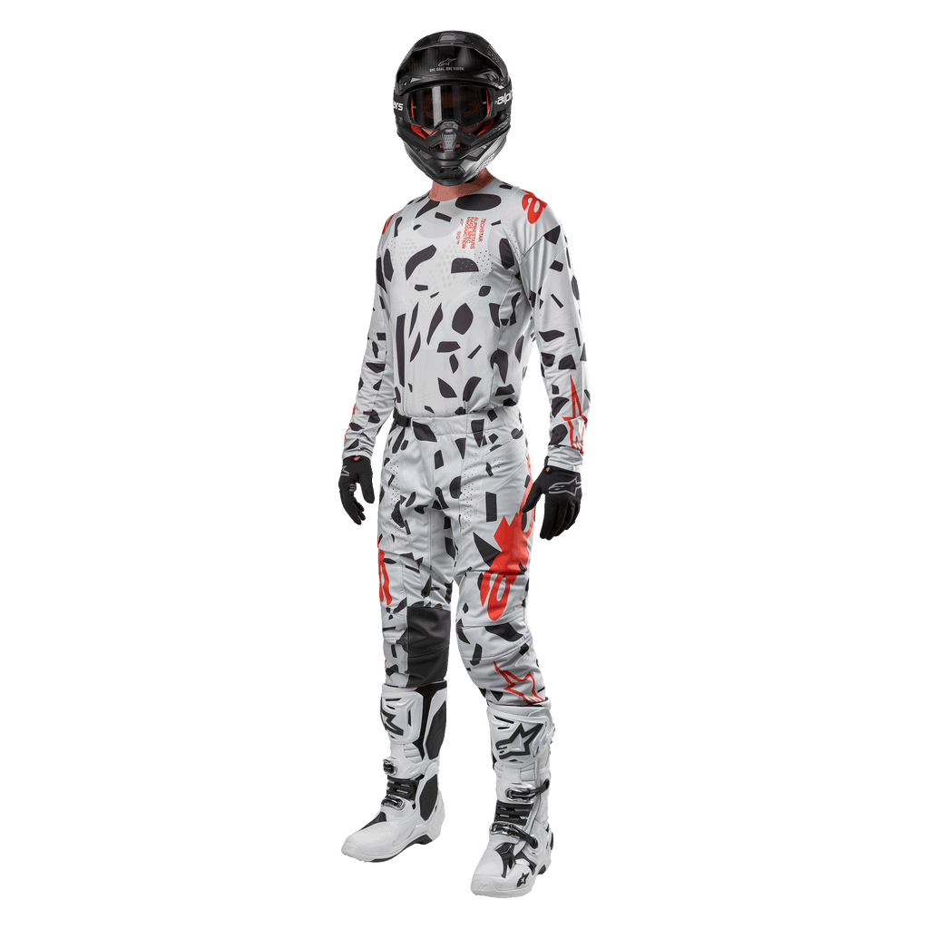 Piloto de motocross con el Alpinestars 2024 Techstar Rantera Jersey en Haze Gray Camo, pantalones a juego con detalles rojos y negros, casco y gafas negras, guantes negros y botas blancas y negras, equipamiento completo de motocross para rendimiento off-road