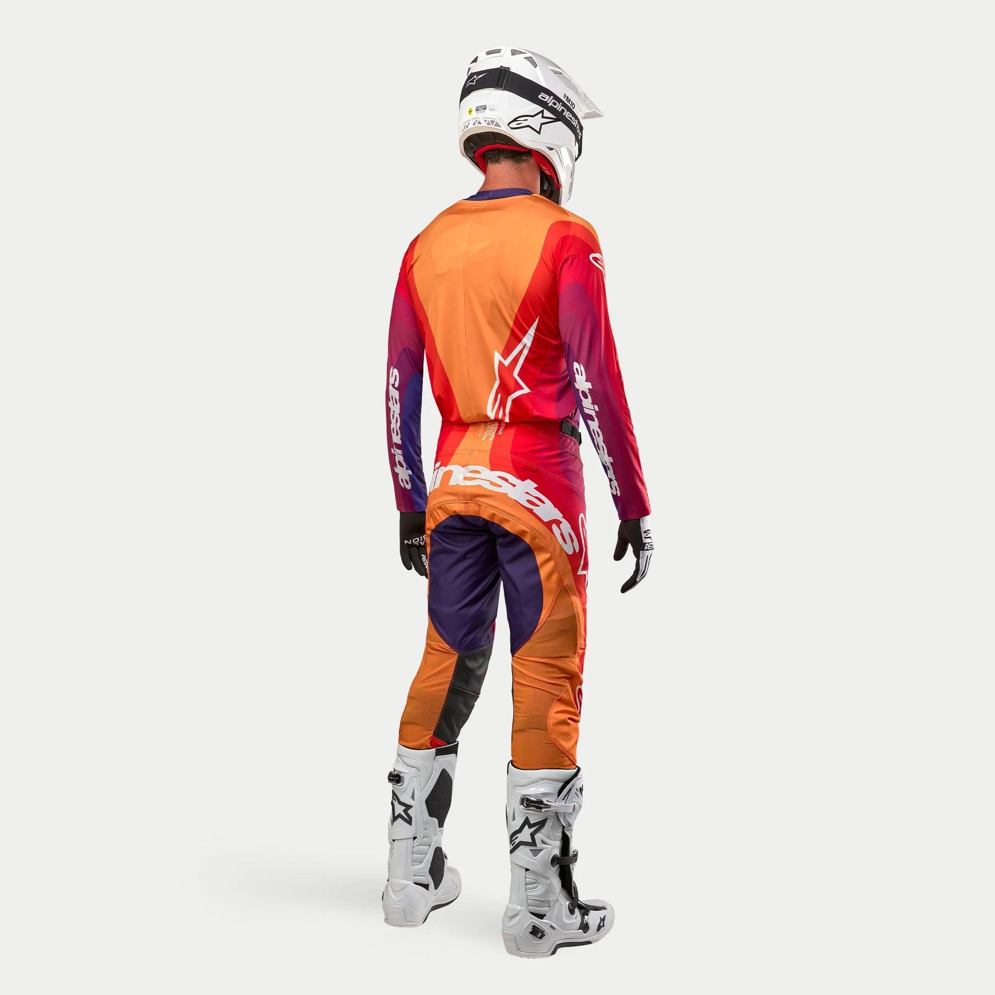 Alpinestars 2024 Techstar Pneuma, conjunto completo de equipamiento de motocross, vista trasera, jersey en tonos naranja y rojo, pantalones en púrpura oscuro, naranja y azul con gran logotipo blanco, casco blanco y botas de motocross blancas