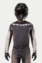 Alpinestars 2024 Techstar Pneuma Jersey, jersey de motocross, arena oscura y gris polvo de hierro, usado con pantalones de motocross a juego y un casco negro, con un destacado logotipo de Alpinestars en el pecho y perforaciones de ventilación cortadas con láser, equipamiento de competición off-road de alto rendimiento.