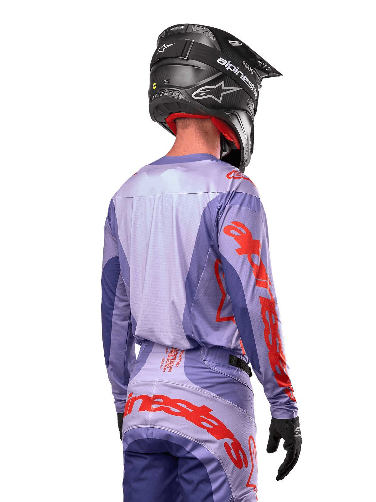 Jersey Alpinestars Techstar Ocuri 2024, jersey de motocross, púrpura y naranja vibrante, vista trasera de un piloto con equipamiento a juego y un casco negro, con grandes letras naranjas de Alpinestars en las mangas y la parte inferior de la espalda