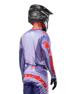 Jersey Alpinestars Techstar Ocuri 2024, jersey de motocross, púrpura y naranja vibrante, vista trasera de un piloto con equipamiento a juego y un casco negro, con grandes letras naranjas de Alpinestars en las mangas y la parte inferior de la espalda