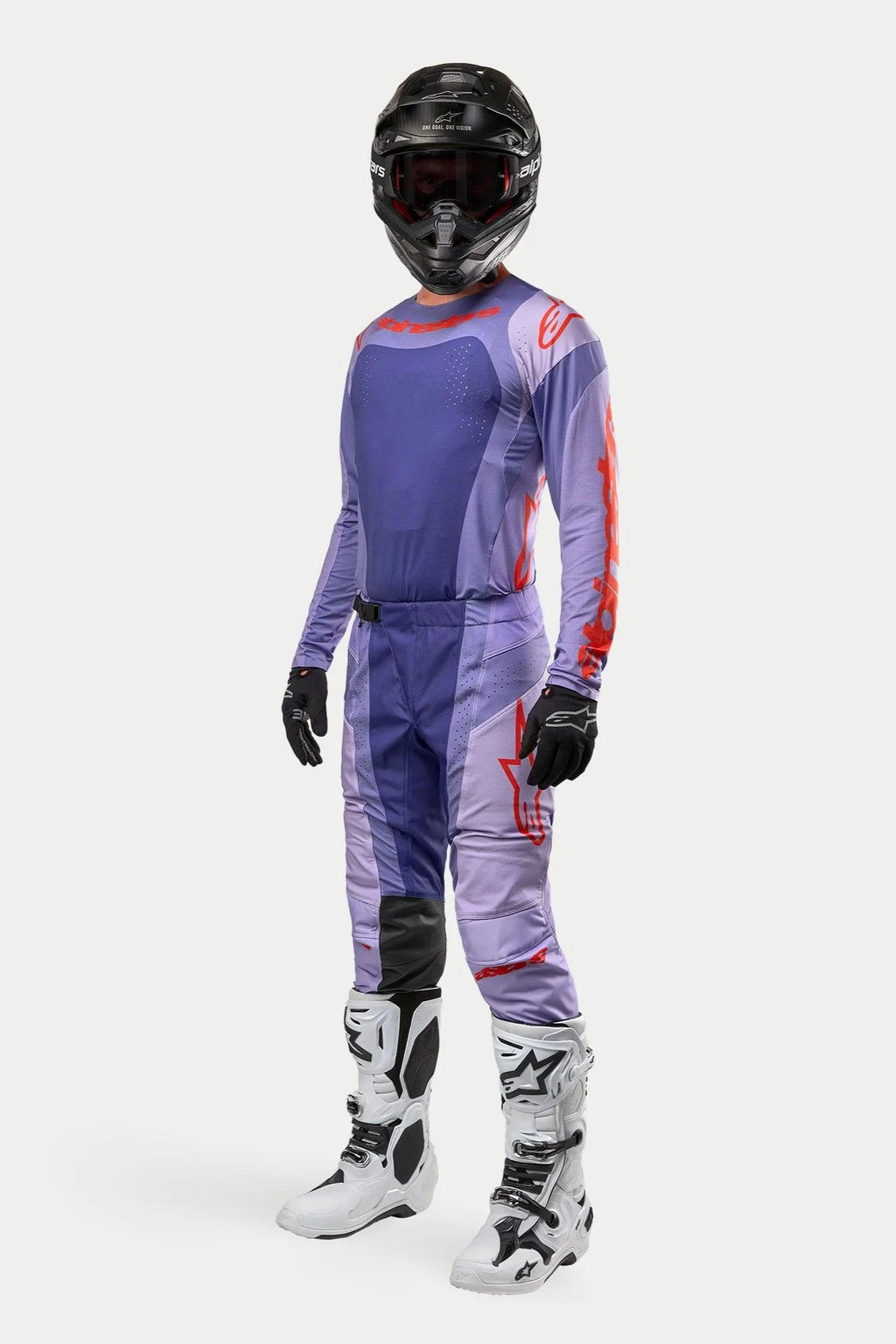 Piloto de motocross con el jersey Alpinestars 2024 Techstar Ocuri en Purple Hot Orange, pantalones de carreras morados a juego con detalles naranja, casco negro, botas blancas y negras, y guantes negros, equipamiento completo de competición todoterreno