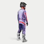Alpinestars 2024 Techstar Ocuri, conjunto completo de motocross, jersey y pantalones en color morado con detalles en naranja vibrante, casco negro, guantes negros y botas blancas con acentos negros, vista posterior que destaca el logotipo de Alpinestars
