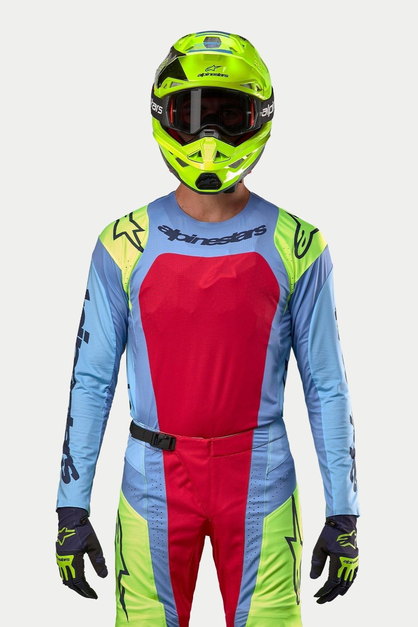 Piloto de motocross con equipamiento completo de competición, Jersey Techstar Ocuri 2024 en azul claro con un gran panel rojo en el pecho y detalles amarillos flúor en los hombros, casco amarillo fluorescente a juego, pantalones coordinados en rojo y amarillo flúor, atuendo profesional para carreras off-road