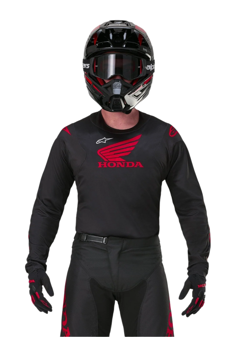 Piloto de motocross con equipamiento completo de carreras, Jersey Honda Racer Iconic negro con el logo de ala roja, pantalones negros a juego con la marca Honda en rojo, casco negro con gafas, y guantes negros y rojos, conjunto coordinado para competición fuera de carretera