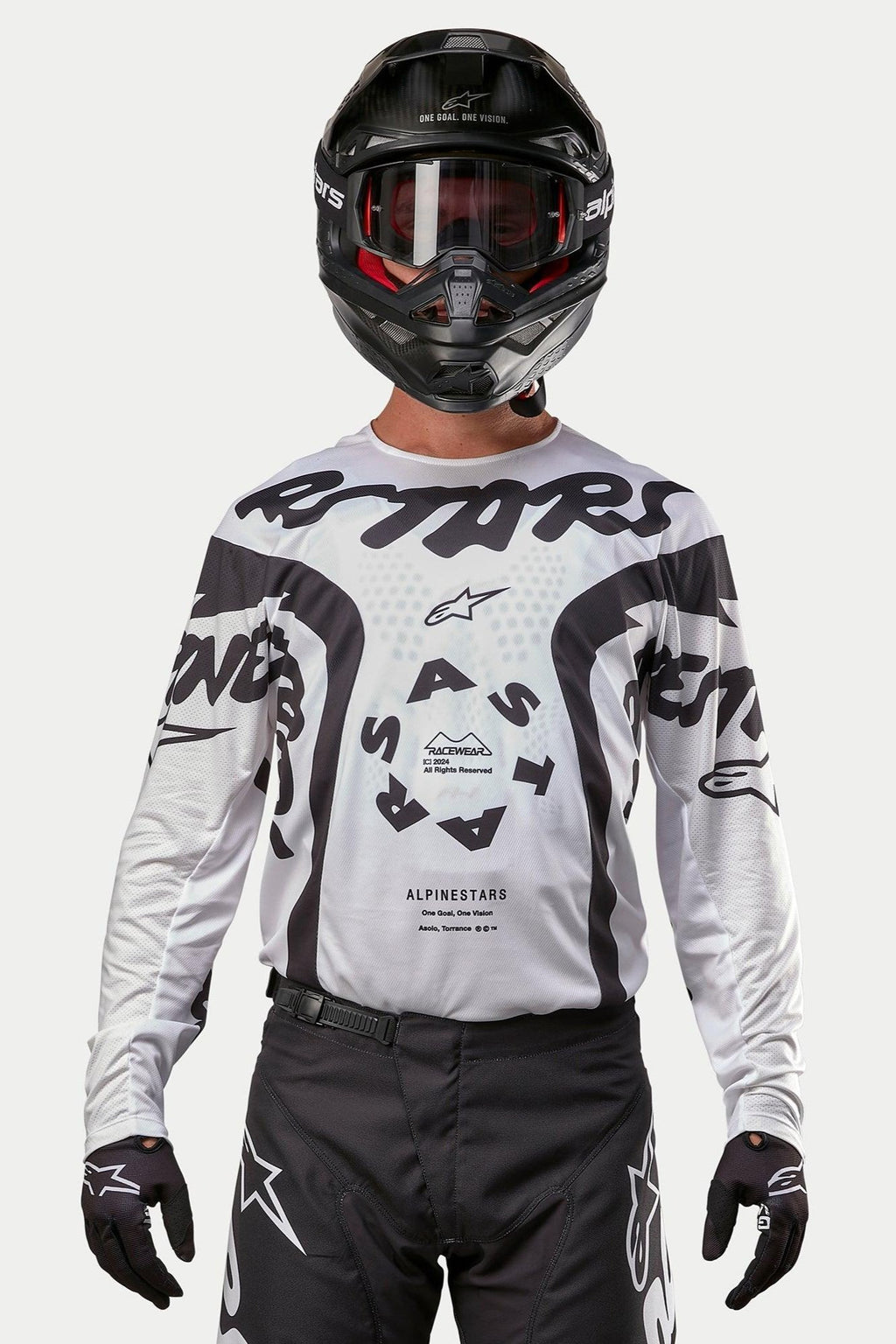 Piloto de motocross con el jersey Alpinestars 2024 Racer Hana en blanco y negro, combinado con casco y pantalones de motocross negros, con gráficos 'ASTARS' destacados y un logotipo central circular, equipamiento profesional para carreras todoterreno