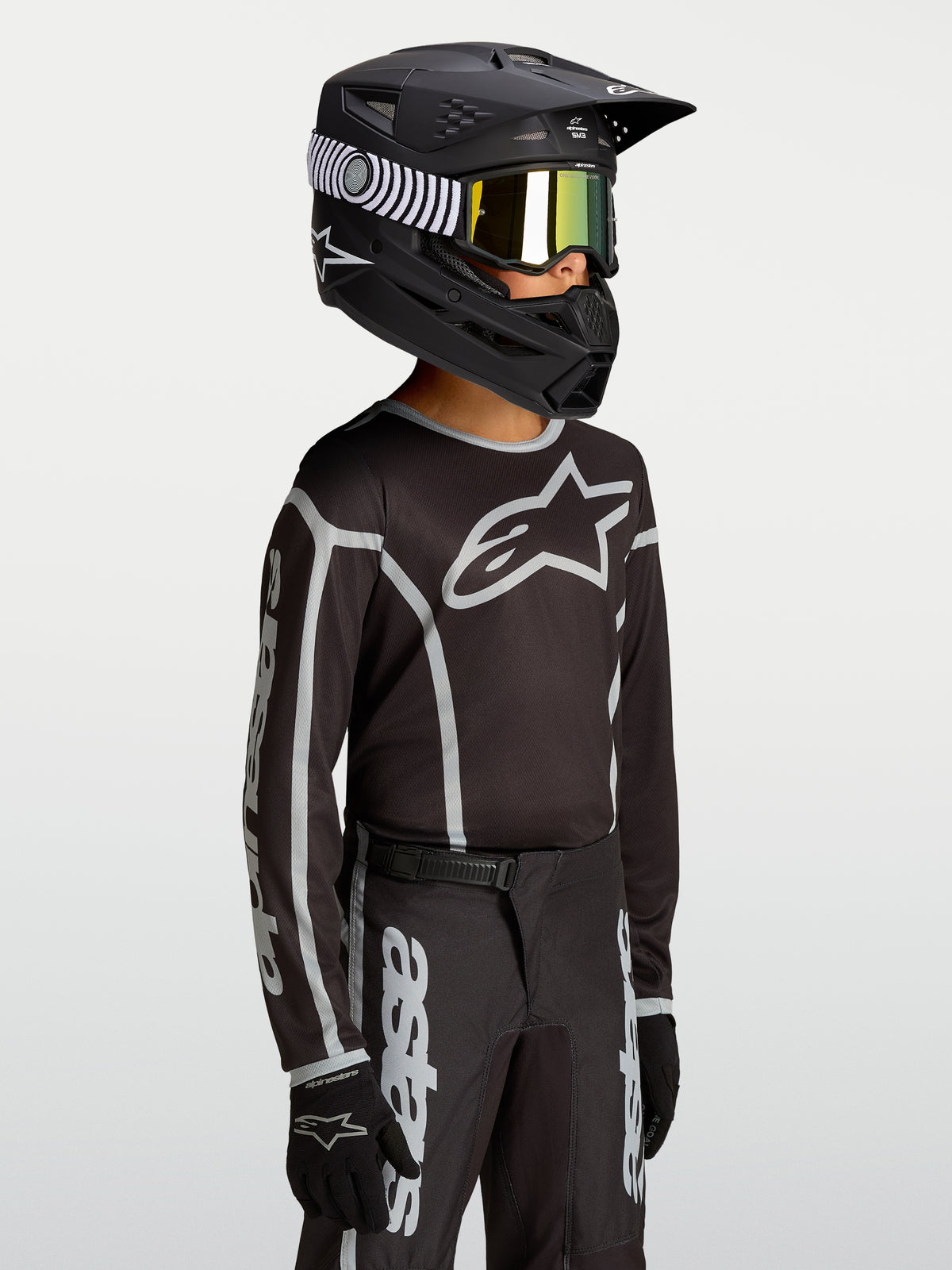 Alpinestars Jersey Fluid Apex V2 Juvenil, para carreras de motocross, juvenil, negro y plateado, tejido técnico transpirable con logotipo, mostrado en modelo joven con casco y equipo completo