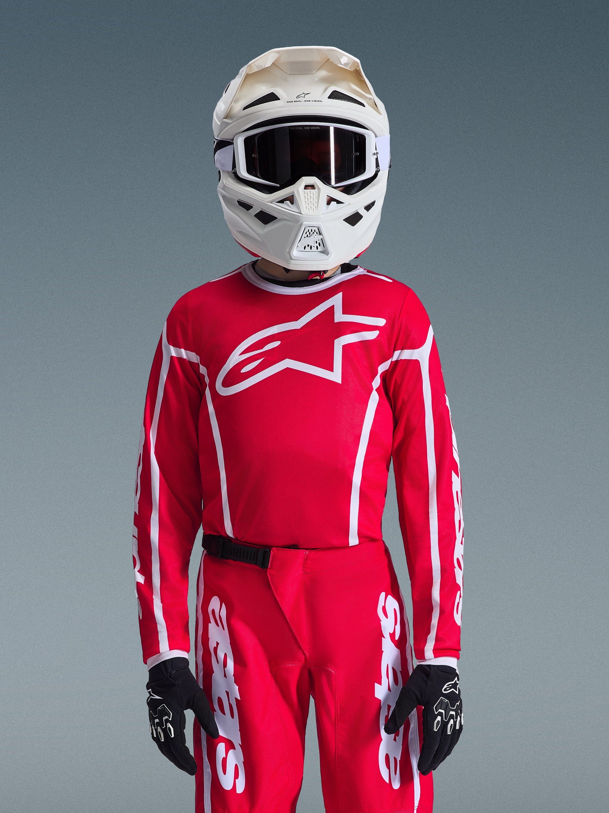Alpinestars 2026 Youth Fluid Apex Jersey, Red and White, worn with matching motocross pants, white helmet with black goggles, and black gloves, featuring a large white logo and athletic fit for youth off-road racing.