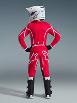 Rear view of a youth motocross rider wearing the Alpinestars 2026 Youth Fluid Apex Jersey in Red and White, matching pants, white helmet with goggles, and black boots, complete off-road racing gear set.