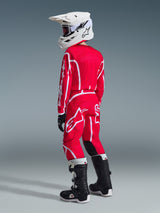 Youth motocross rider wearing complete racing gear, Alpinestars 2026 Youth Fluid Apex Jersey in Red and White, matching red pants with white logos, white helmet, and black and white boots, back view, coordinated outfit for off-road racing
