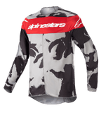 Alpinestars Youth 2023 Racer Tactical Jersey, jersey de motocross, camuflaje Gris Cast y Rojo Mars, con una banda roja horizontal en el pecho y el logotipo blanco de Alpinestars, patrón de camuflaje gris y negro, tejido ligero que absorbe la humedad para conducción off-road