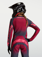 Alpinestars Stella Techstar Swan Jersey, jersey de motocross para mujer, rojo carmesí y gris oscuro, tejido elástico transpirable, vista trasera en modelo con casco.