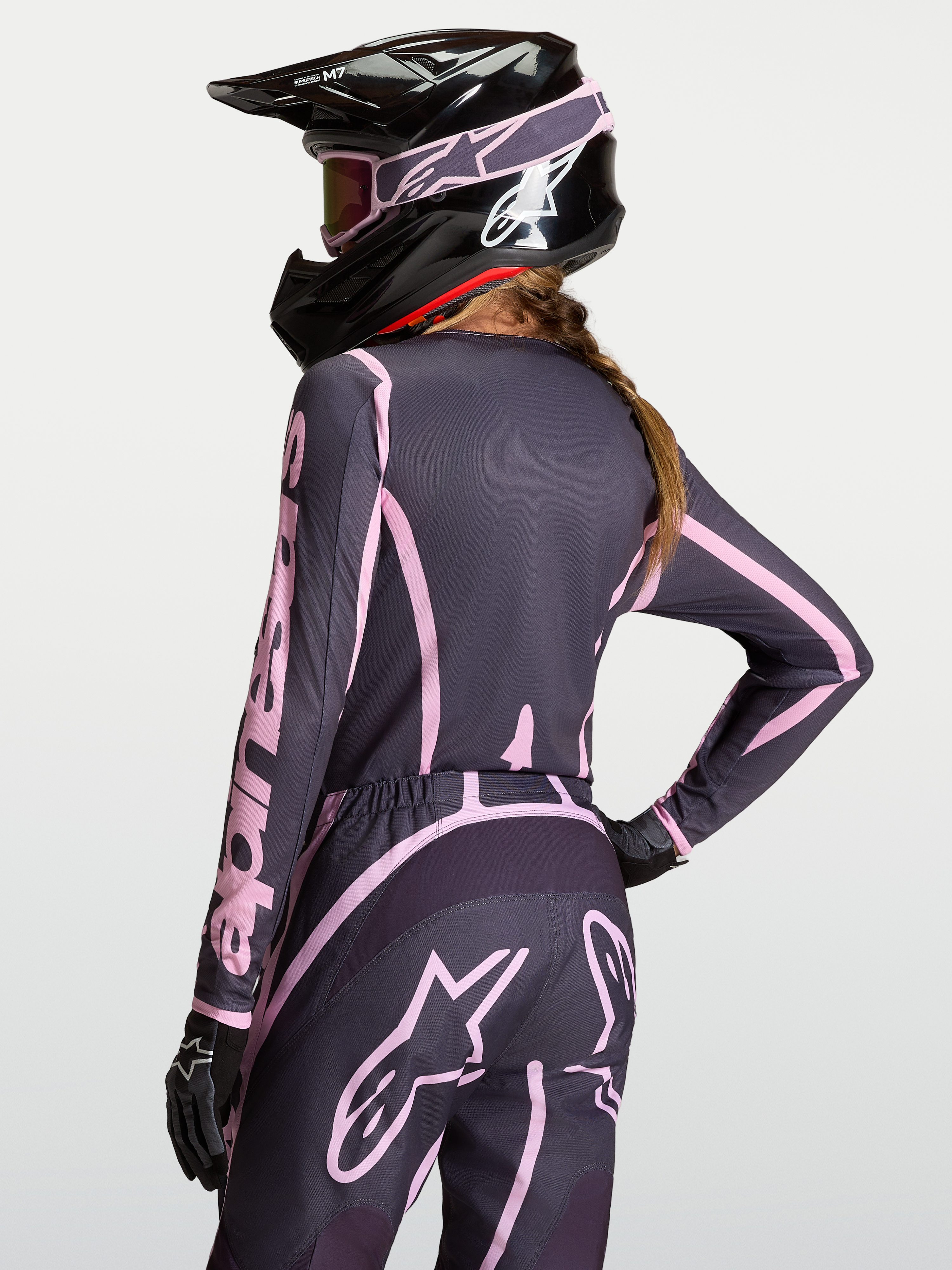 Alpinestars Stella Fluid Apex V2, jersey de motocross para mujer, gris y rosa, con casco negro, vista trasera en modelo