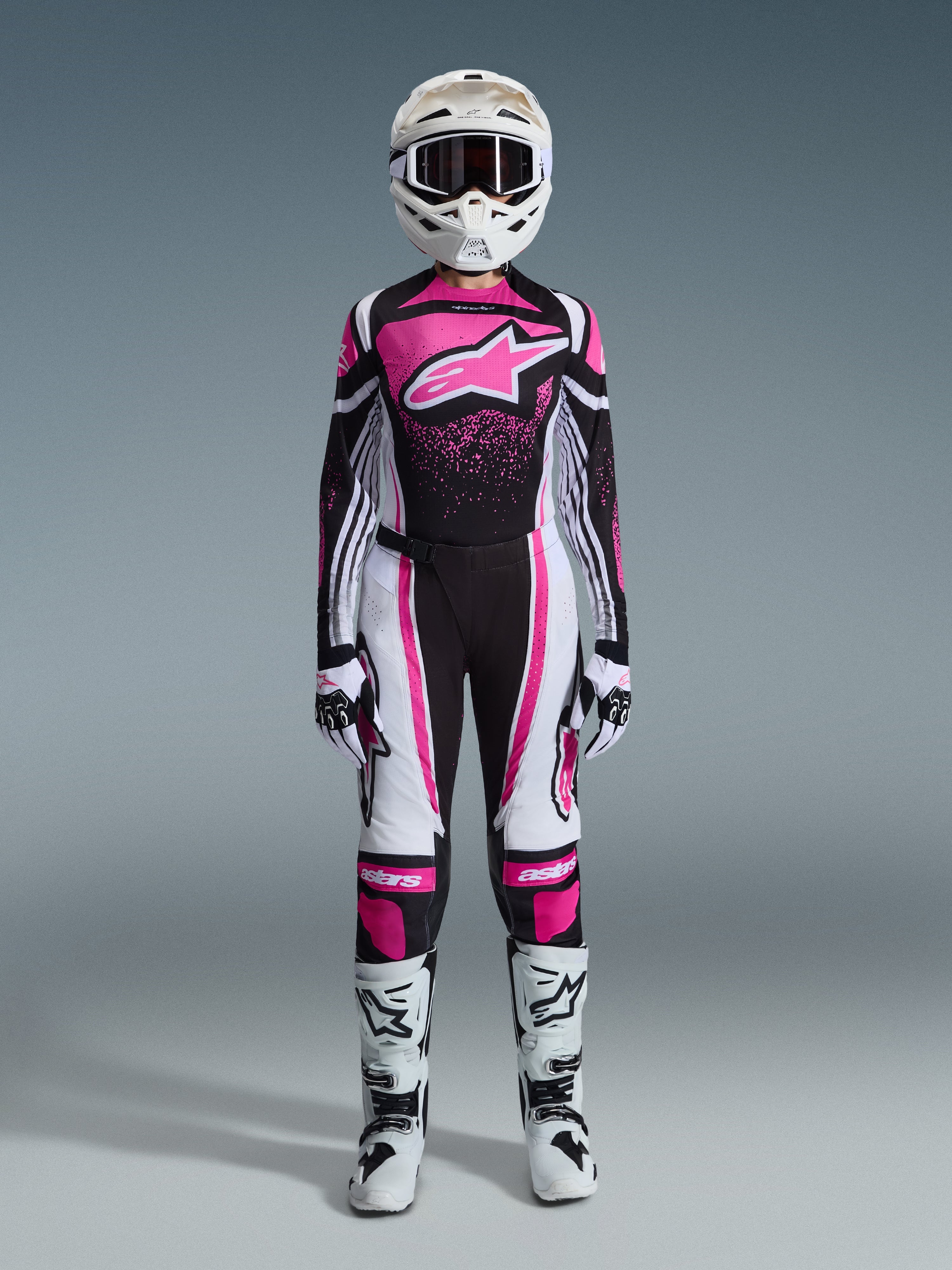 Alpinestars Stella Techstar Nomur 2026 para mujer, conjunto completo de equipo de motocross, traje de carreras en negro, blanco y fucsia, jersey con un gran logo de estrella y diseño de salpicaduras rosas, pantalones a juego, casco blanco con gafas, botas blancas y negras, equipamiento de off-road coordinado para mujer