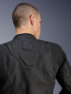 Chaqueta de cuero Alpinestars Dusk, negro, primer plano de la parte superior de la espalda y los hombros con el logotipo DUSK grabado en relieve en un panel acolchado, inserciones elásticas de cuero en acordeón, confeccionada en cuero bovino de primera calidad