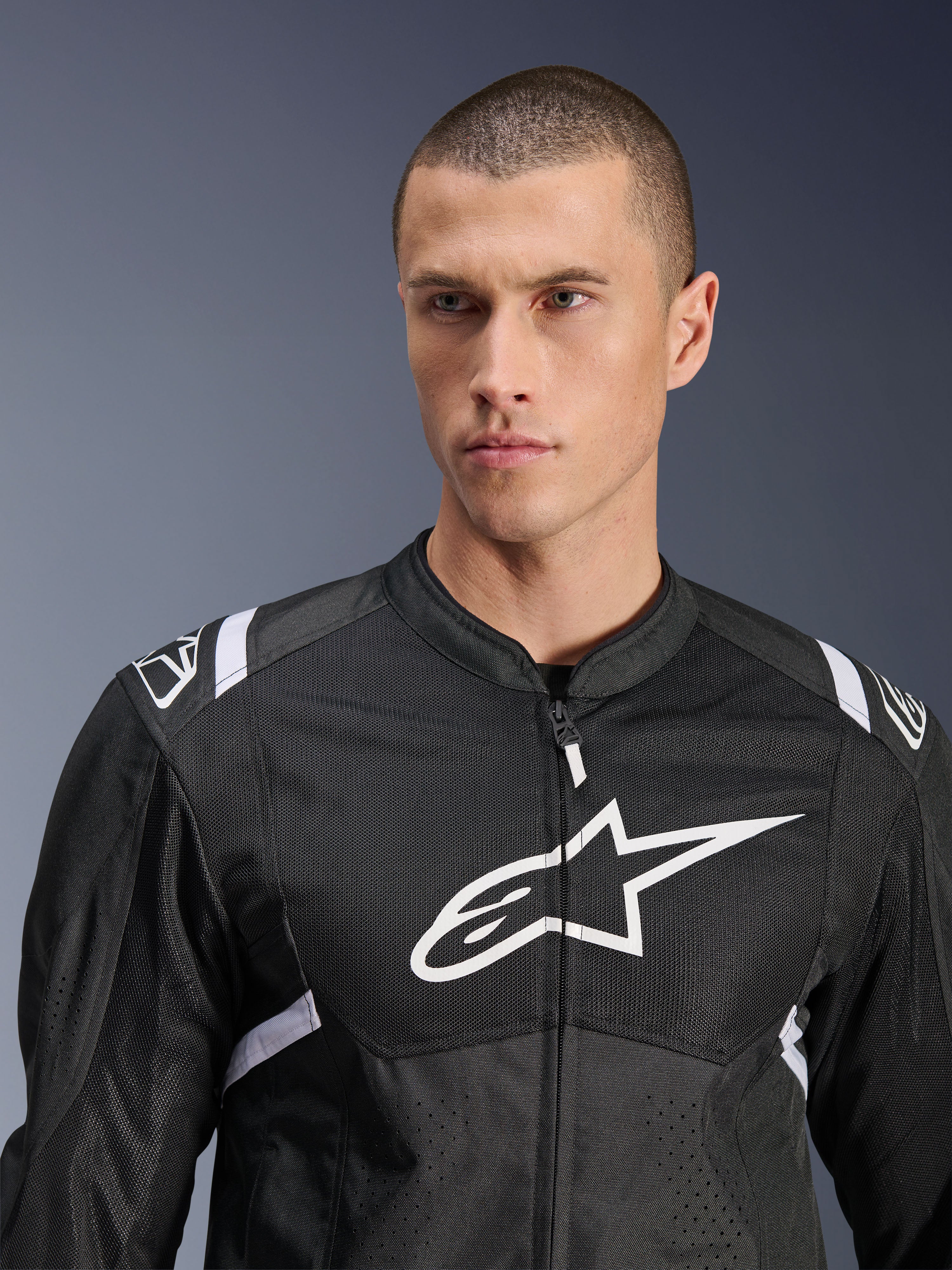 Chaqueta Alpinestars T-SPS Air V2, chaqueta de moto textil, negra y blanca, con un gran logotipo blanco en el pecho y paneles de malla, ajuste deportivo de alto rendimiento usada por un modelo masculino