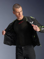 Modelo masculino vistiendo la chaqueta Alpinestars T-Sps Air V2 en negro y amarillo flúor, mostrada abierta para resaltar la construcción interna de malla y los bolsillos, combinada con una prenda técnica Alpinestars negra y pantalones negros, estilo de equipamiento urbano para motociclista