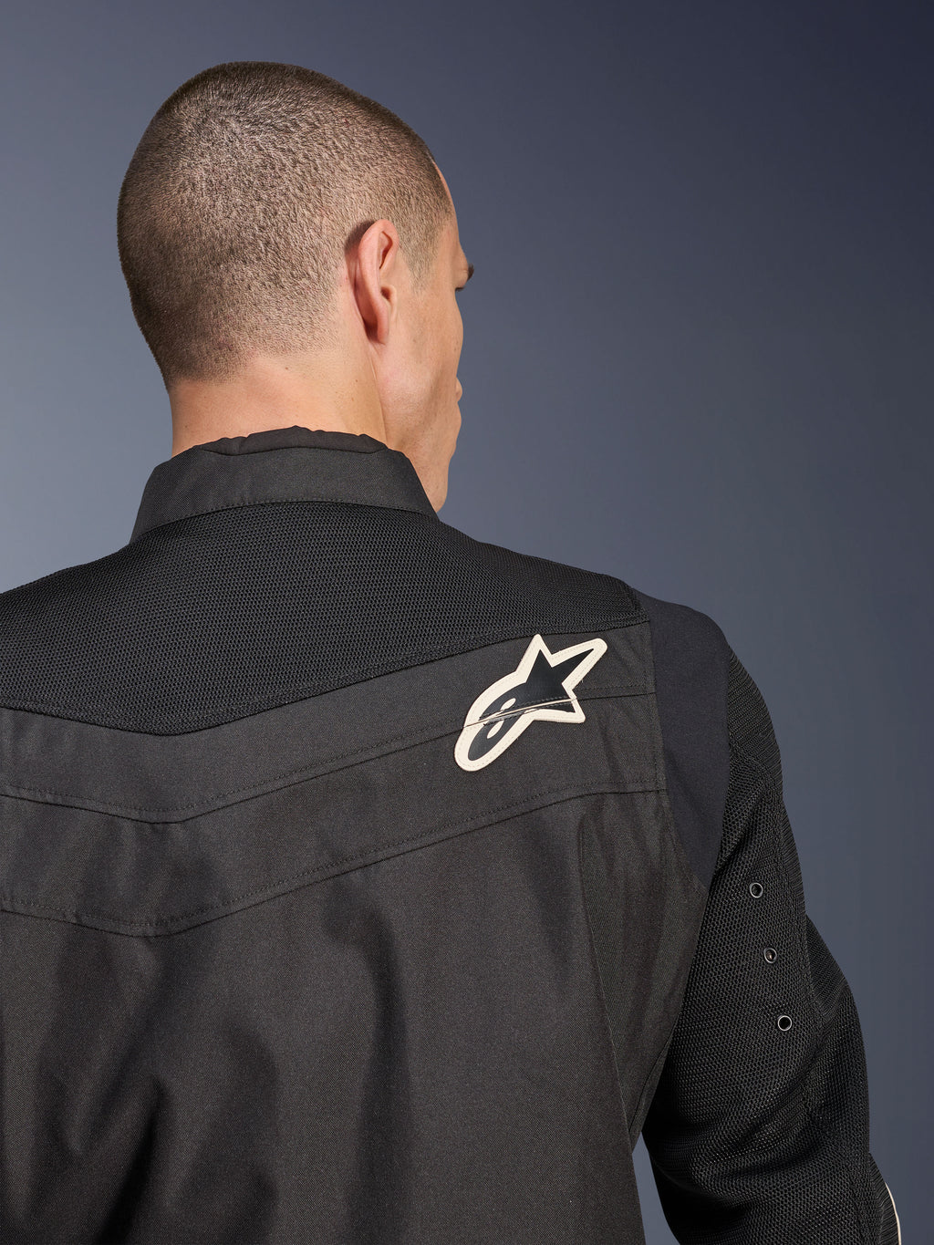Chaqueta Alpinestars T-Dyno Air, chaqueta de moto textil negra, vista trasera en primer plano que destaca el canesú y las mangas de malla 3D transpirable, con un logotipo de estrella en blanco y negro en el hombro derecho.