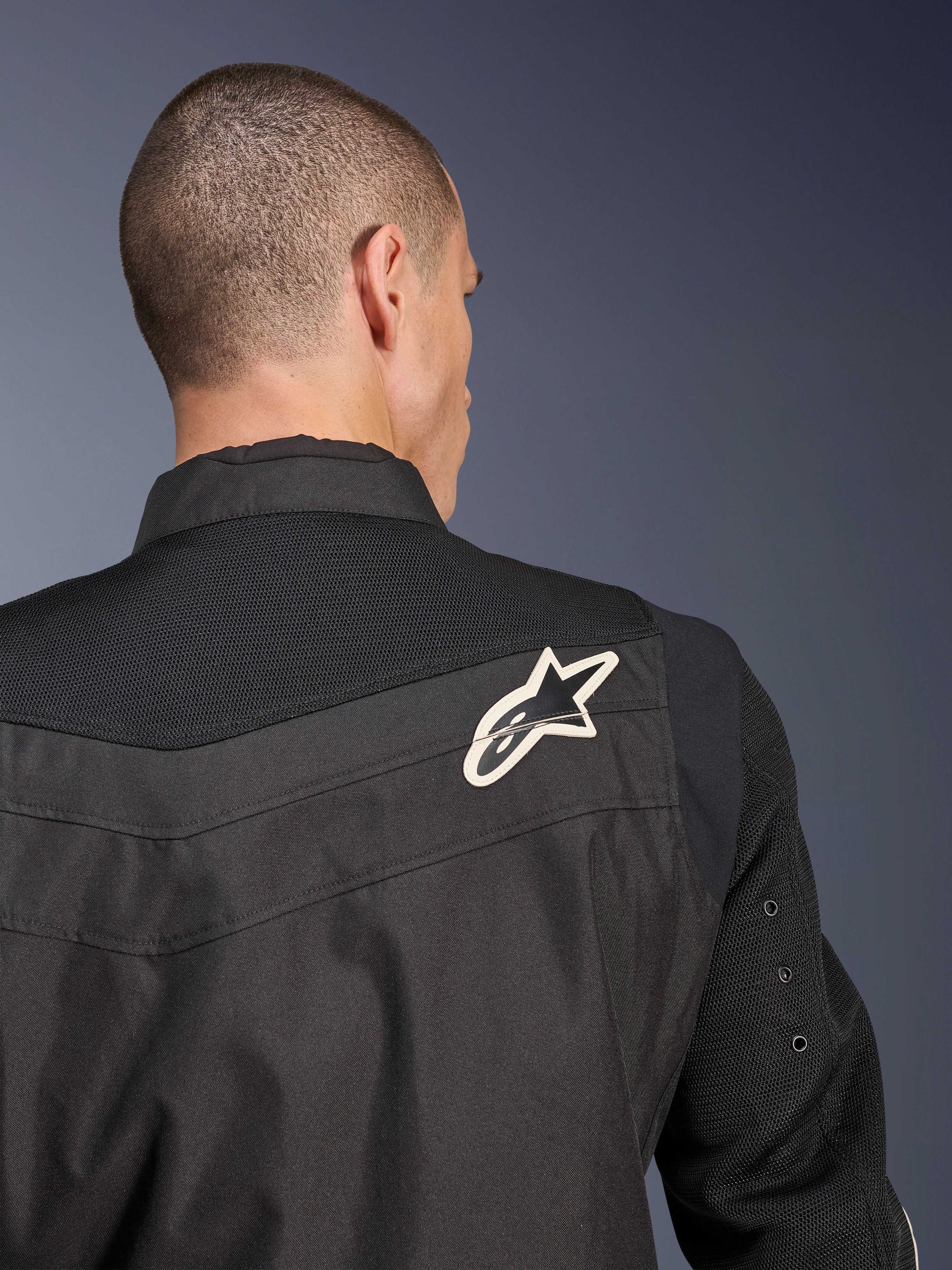 Chaqueta Alpinestars T-Dyno Air, chaqueta de moto textil negra, vista trasera en primer plano que destaca el canesú y las mangas de malla 3D transpirable, con un logotipo de estrella en blanco y negro en el hombro derecho.