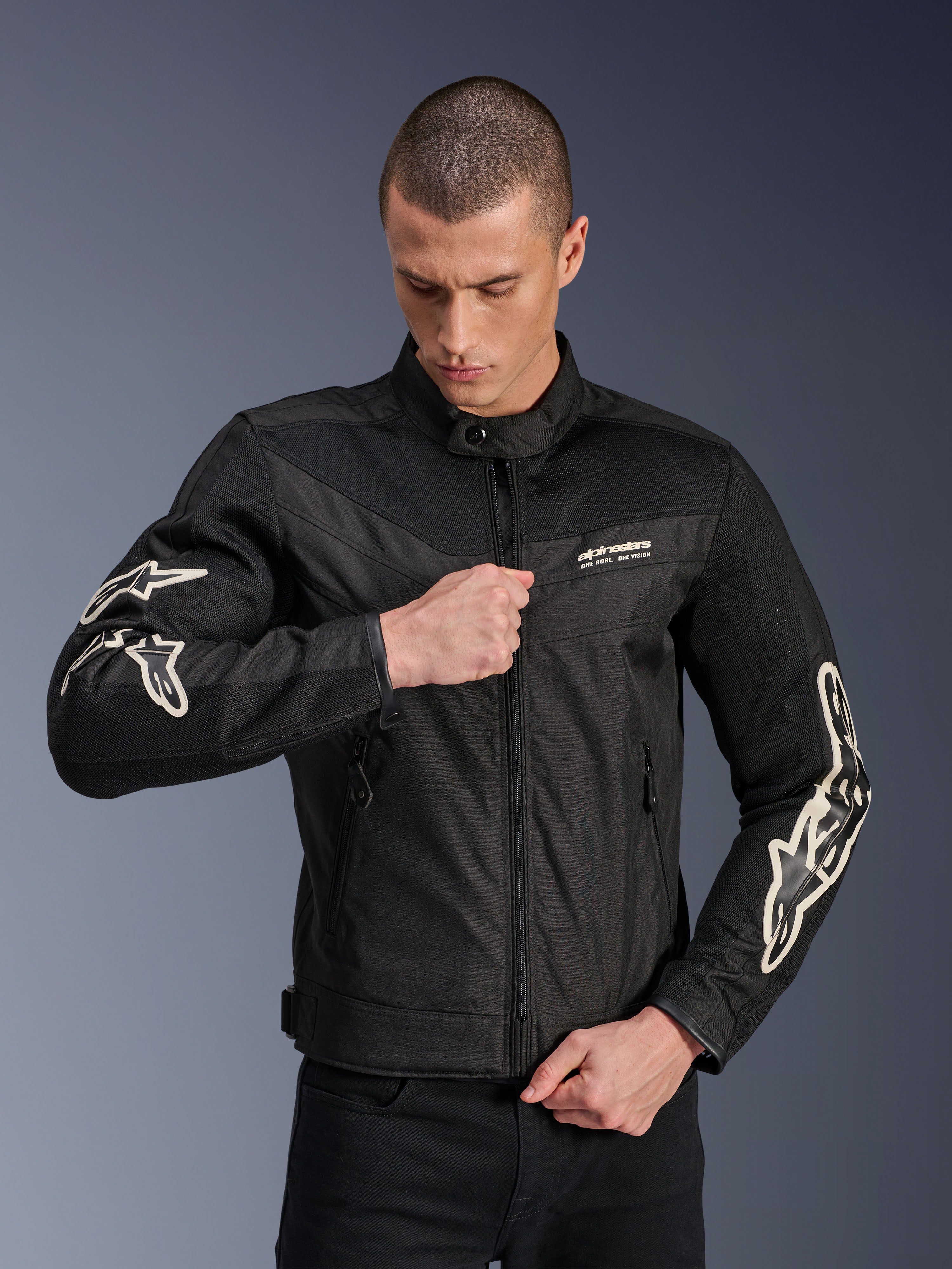 Chaqueta Alpinestars T-Dyno Air, negra, chaqueta de moto textil con paneles de malla 3D y logotipos blancos en las mangas, usada por un modelo subiendo la cremallera frontal, estilo de conducción urbano