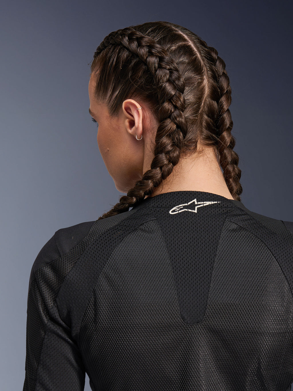 Chaqueta Stella Troop-Air de Alpinestars para mujer, negra, vista detallada posterior de la parte superior de la espalda y el cuello, mujer con trenzas francesas, con un logotipo de Astars blanco en el cuello y tejido de malla técnica 2D ligera para ventilación