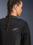 Alpinestars Stella T-Dyno Air Jacket, chaqueta de moto negra para mujer, vista de cerca de la parte posterior que muestra los paneles de malla 3D en el canesú y la parte superior de la espalda para el flujo de aire, con un pequeño logotipo de estrella blanco, lucida por una modelo con el cabello trenzado.