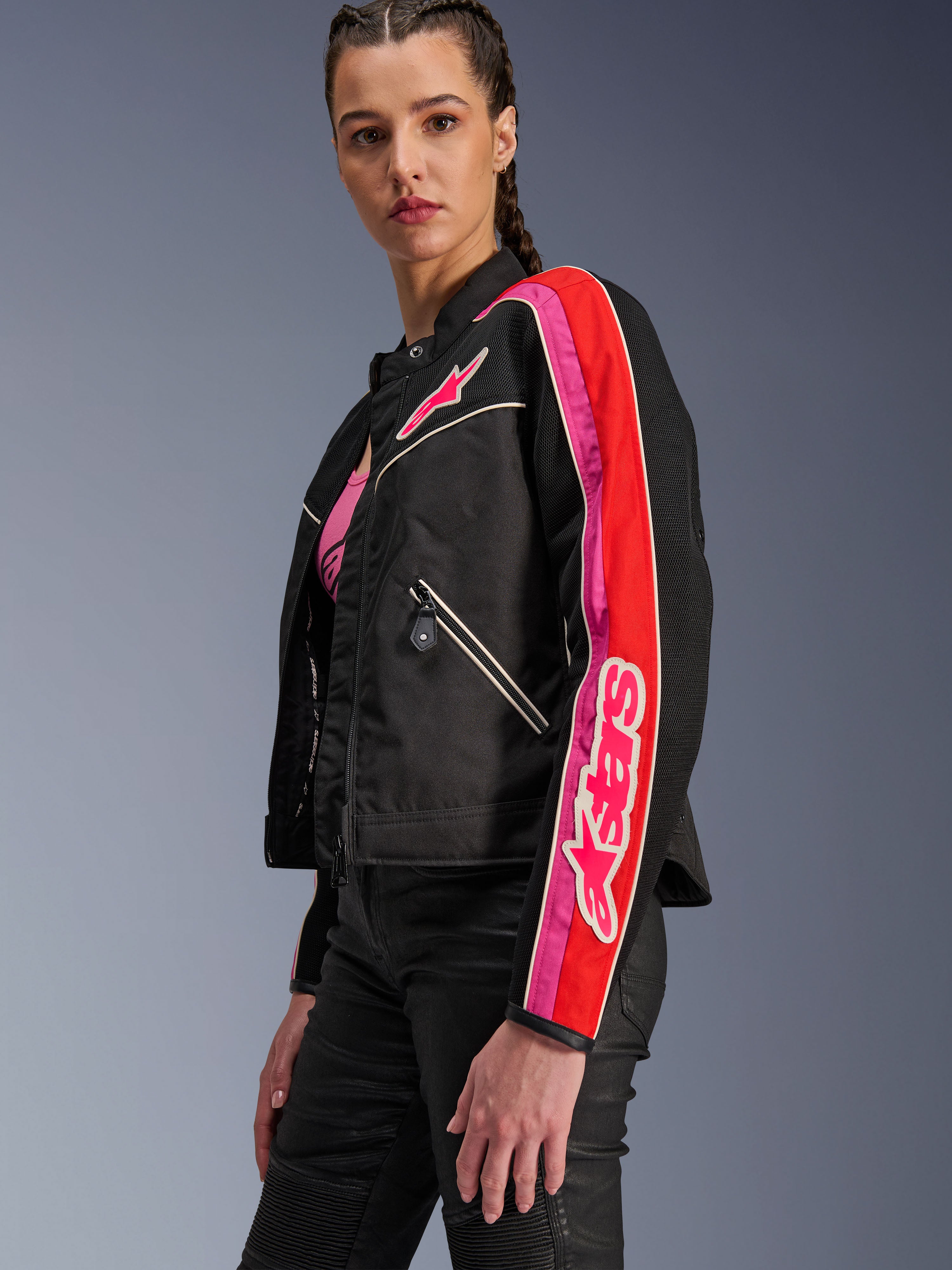 Chaqueta Alpinestars Stella T-Dyno Air para mujer, chaqueta de moto para mujer, negra con detalles en rojo brillante y fucsia, usada con pantalones negros, con el logotipo Astars rosa en el pecho y la manga, ajuste de motociclista entallado con paneles de malla para ventilación.