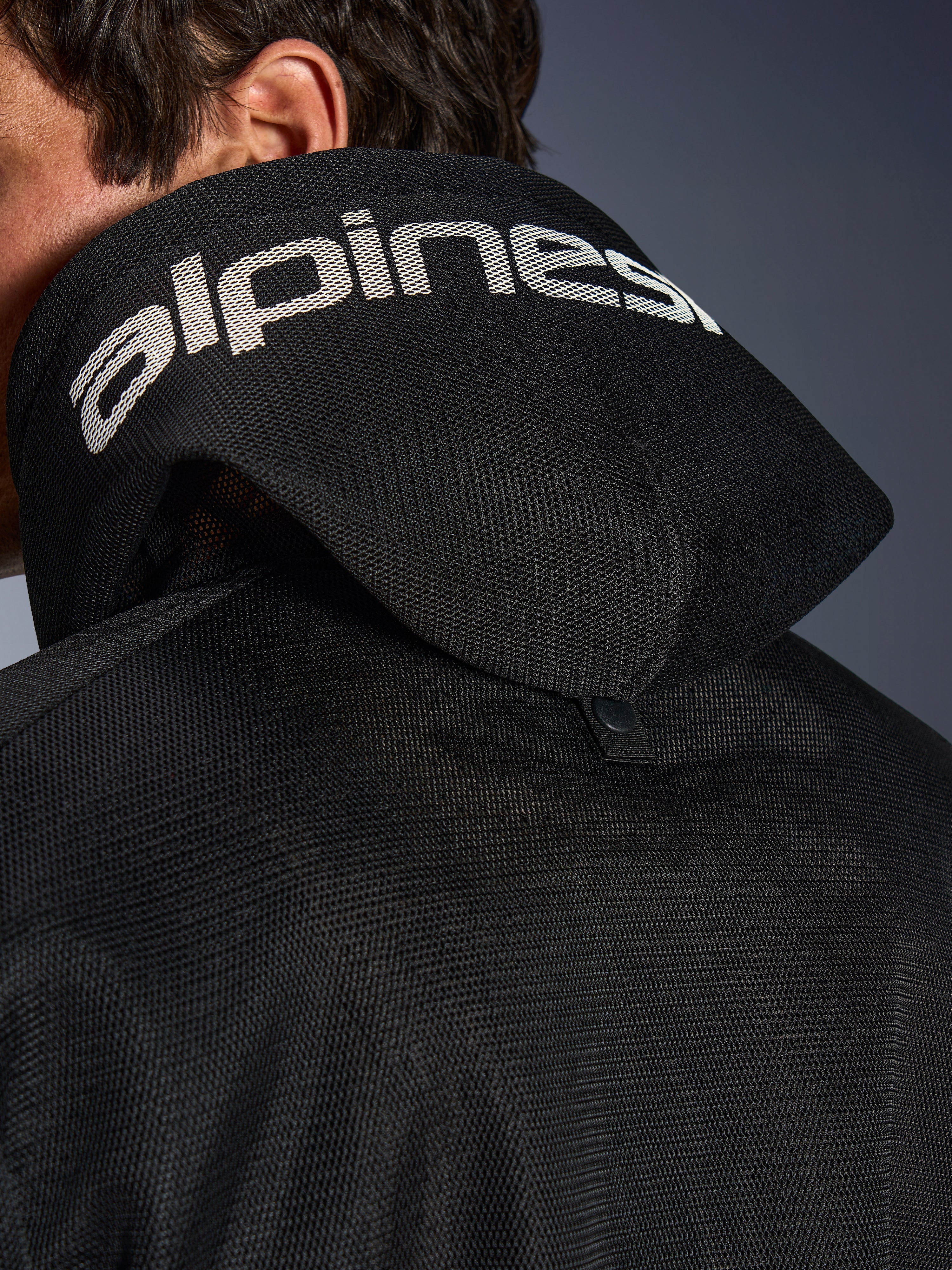 Alpinestars Chrome Superairflow Hoodie, negra, vista de detalle de la capucha de malla 3D con logotipo de Alpinestars en blanco, botón de presión de estabilización trasero, equipamiento textil ventilado para moto en condiciones de calor extremo