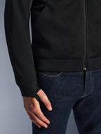Alpinestars Chrome Superairflow Hoodie, negra, primer plano del tejido de malla técnica 3D de alta resistencia, con puño de punto jersey elástico acanalado y lazo para el pulgar, combinada con vaqueros azules