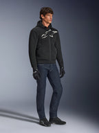 Sudadera con capucha Alpinestars Chrome Superairflow, negra con logotipo en blanco y gris, construcción textil de malla 3D ventilada, combinada con vaqueros denim azul oscuro y guantes de moto negros, estilo de conducción deportiva urbana.