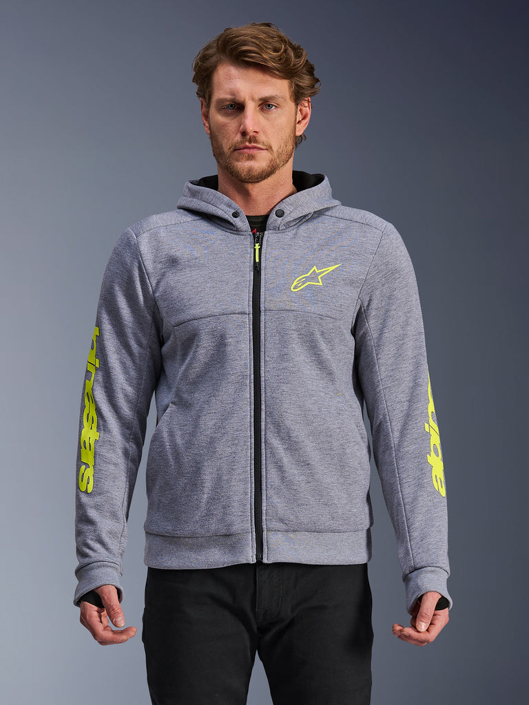 Sudadera Alpinestars Chrome V2 Sport, gris jaspeado y amarillo flúor, vista frontal en modelo, sudadera de moto en forro polar técnico con cremallera frontal, logo de estrella en amarillo neón en el pecho y marca en las mangas, equipamiento casual de conducción urbana