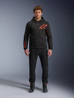 Sudadera Alpinestars Chrome Air Sport, negro y rojo flúor, chaqueta urbana para motociclista con construcción de tejido polar técnico, con un gran logotipo rojo de Astars en el pecho y marca en la manga, lucida por un modelo con pantalones negros y calzado de moto