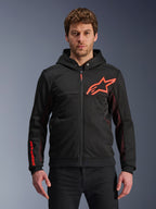 Alpinestars Chrome Air Sport Hoodie, sudadera negra con cremallera y capucha con logotipo de estrella en rojo flúor y detalles en las mangas, paneles laterales de malla roja para ventilación, equipamiento de conducción urbana casual usado por un modelo