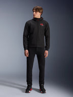 Alpinestars MM93 Radium Tech Hoodie, sudadera urbana de moto en color negro, con el logotipo 93 en rojo y el logotipo de la estrella en blanco en el pecho, lucida por un modelo con pantalones negros y calzado de moto a juego, prenda técnica cortavientos para conducción urbana