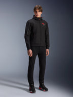 Sudadera con capucha Alpinestars MM93 Radium Tech, chaqueta de moto urbana, negra con detalles en rojo brillante, usada por un modelo con pantalones negros y calzado de moto, con el logotipo '93' rojo en el pecho y la marca Marc Márquez en la manga, ropa técnica casual para conducción urbana