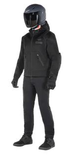 Sudadera con capucha Alpinestars Moflow Air Tech, sudadera urbana para moto, color negro, usada por un piloto con casco negro mate, guantes negros y pantalones de conducción, con una confección íntegra en malla para el flujo de aire, bolsillos con cremallera y logotipos sutiles en el pecho, diseño casual y elegante para conducción urbana en climas cálidos.