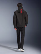 Sudadera con capucha Alpinestars Radium Tech, chaqueta de moto urbana, color negro, vista trasera con el texto 'ALPINE' en rojo brillante en la capucha, combinada con pantalones negros y zapatillas, elegante carcasa técnica para desplazamientos urbanos.