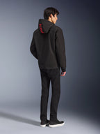 Alpinestars Radium Tech Hoodie, negra con la marca Alpinestars en rojo en la capucha, vista trasera en un modelo masculino con pantalones negros y zapatillas, equipamiento técnico para conducción urbana