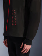 Alpinestars Radium Tech Hoodie, chaqueta de moto urbana, negro y rojo brillante, primer plano del gráfico frontal con texto vertical en rojo "ALPINESTARS ONE GOAL ONE VISION", cremallera roja y puño acanalado con orificio para el pulgar.