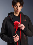 Sudadera con Capucha Alpinestars Radium Tech, chaqueta de moto urbana, negro y rojo brillante, usada por un modelo que muestra un protector de pecho rojo, cuenta con cremalleras en rojo brillante y marca Alpinestars vertical, capa técnica cortavientos para uso urbano