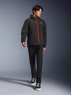 Alpinestars Radium Tech Hoodie en Black Bright Red, chaqueta de moto urbana usada por un modelo, con una cremallera frontal roja y el logo en el pecho, combinada con pantalones negros y zapatillas para un look moderno de trayecto diario.