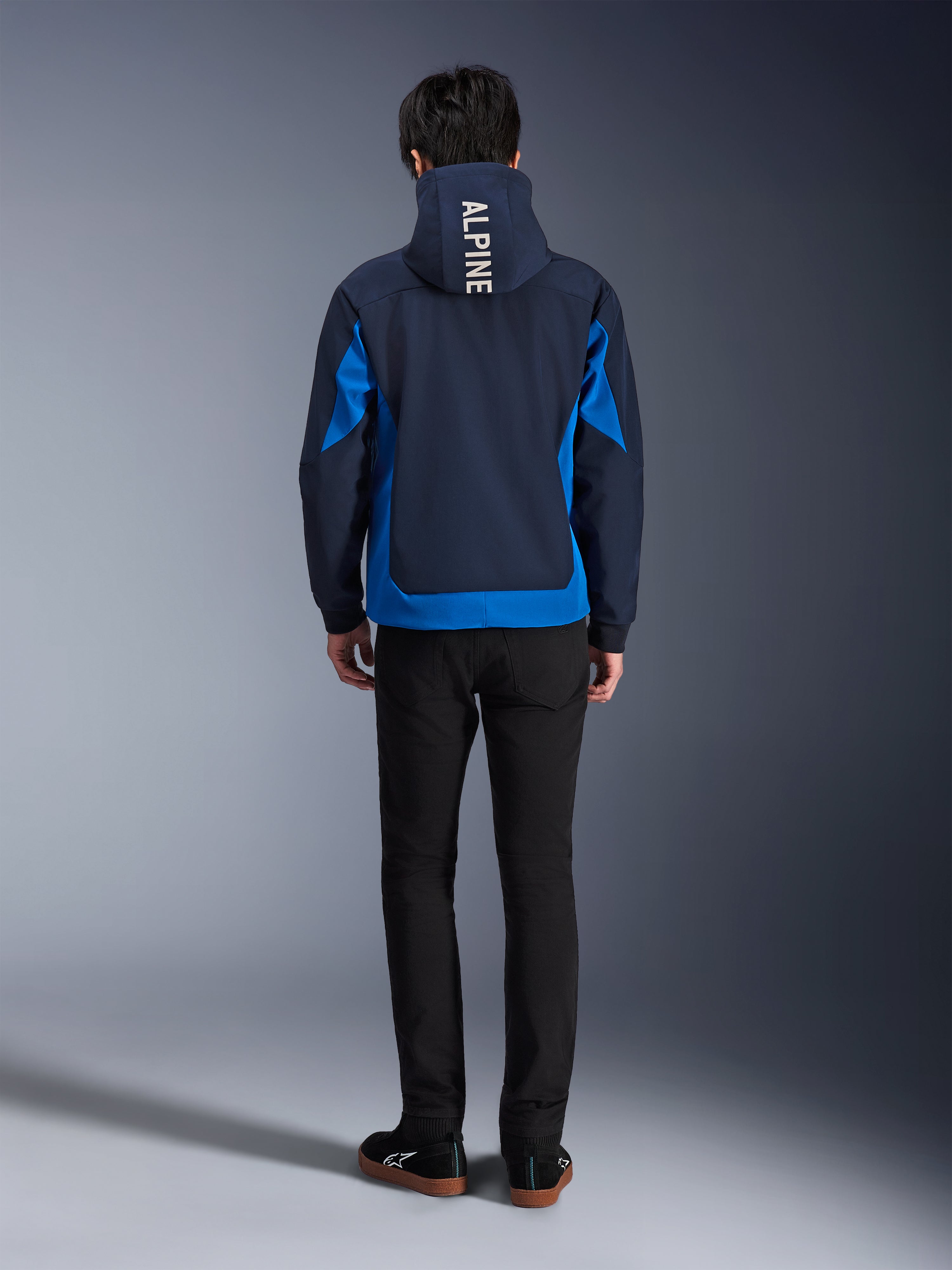 Alpinestars Radium Tech Hoodie, Night Navy and Royal Blue, back view showing vertical 'ALPINE' branding on the hood, royal blue side panels and hem, casual urban motorcycle hoodie with windproof 3L shell, worn with black pants