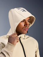 Alpinestars Radium Tech Hoodie en Mastic Aluminum, primer plano de un hombre con la capucha puesta, con el logotipo de Alpinestars en la parte superior, chaqueta de moto urbana con capa técnica cortavientos, estética streetwear moderna para conducción en ciudad