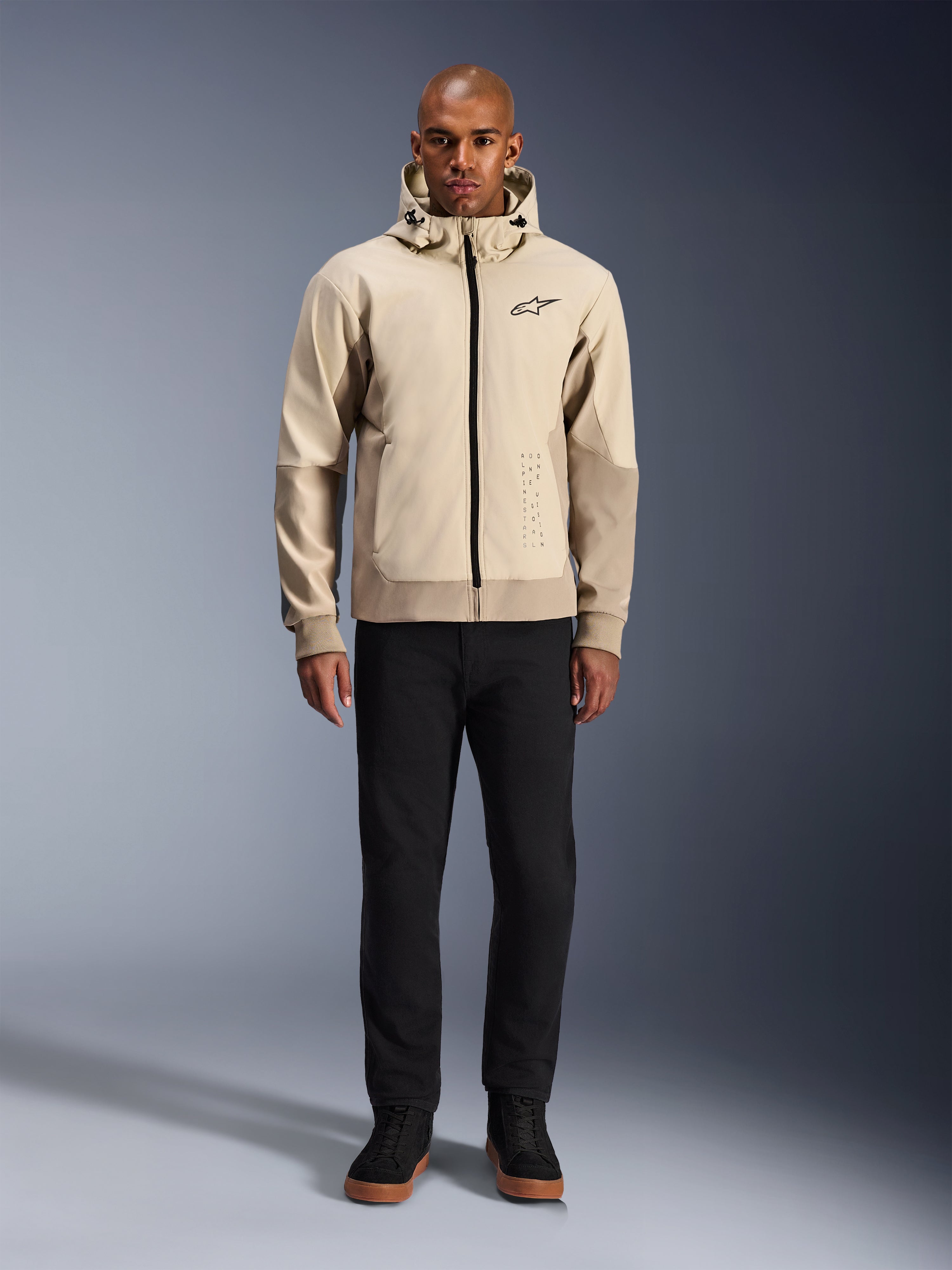 Alpinestars Radium Tech Hoodie en Mastic Aluminum, sudadera urbana para motociclista usada por un modelo masculino con pantalones y botas negras, con cremallera negra completa, logotipo pequeño en el pecho y ajuste atlético para conducción en ciudad.