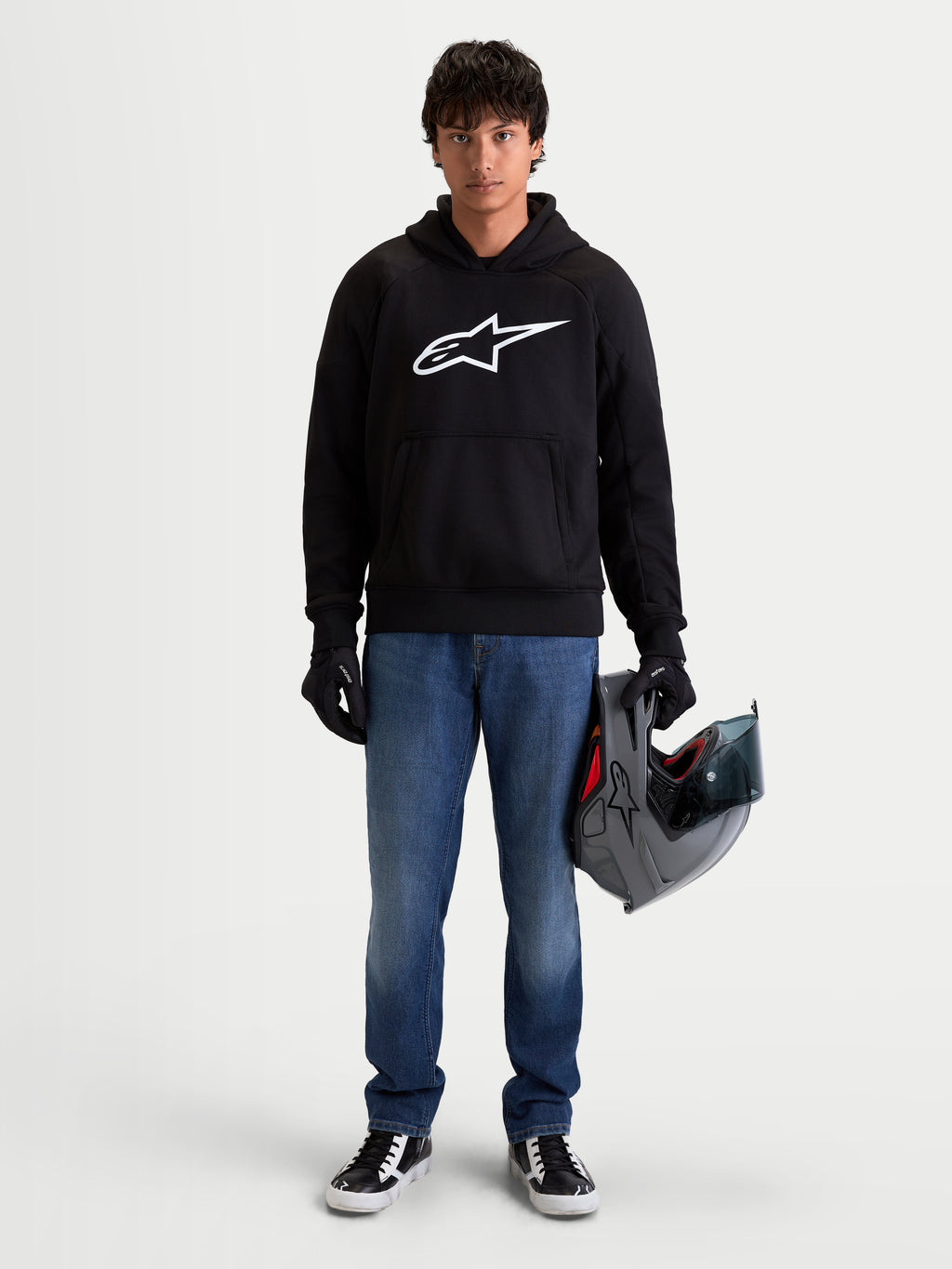 Alpinestars Ageless Hoodie, men's urban motorcycle hoodie in black with a prominent white Astar logo on the chest, worn by a model holding a helmet and wearing riding gloves, casual CE certified protective motorcycle apparel.