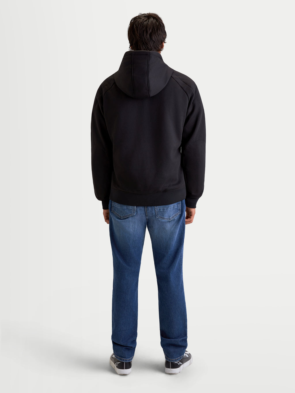 Alpinestars Ageless Hoodie, men's urban motorcycle hoodie in black, rear profile view on a model wearing jeans and casual riding shoes, featuring a fixed hood and protective textile construction.